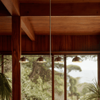 Clérachic four-dome bar pendant light in chrome, hung beneath heavy timber beams before a fixed glazed wall framing trees and a distant sea horizon.