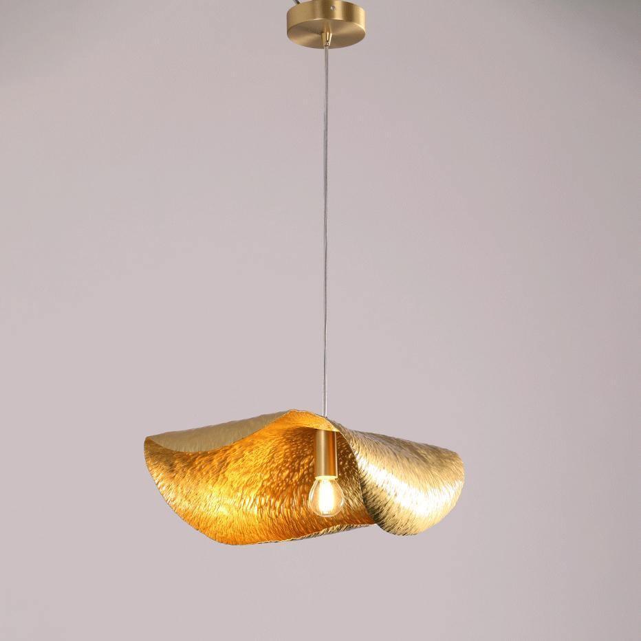 A single hammered brass shade from Clérachic glows gold against a plain grey studio backdrop.