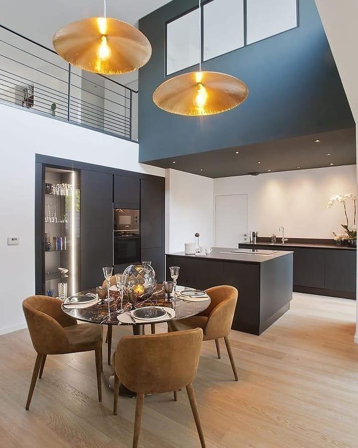 Two lit Clérachic pendants hang in a two-storey dining space beside a deep blue wall.