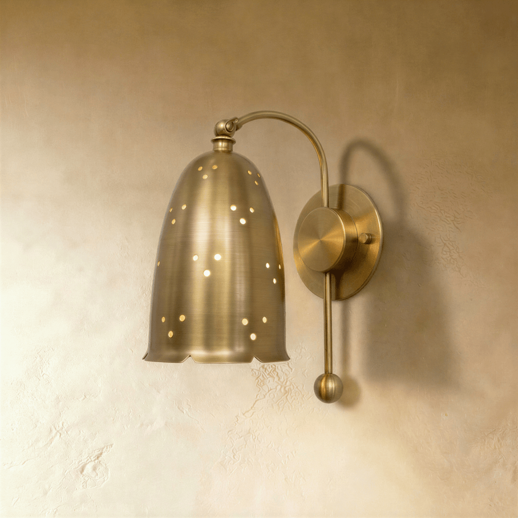 Clérachic wall lamp in brushed brass, the perforated bell shade curved on a slender wall-mounted arm.