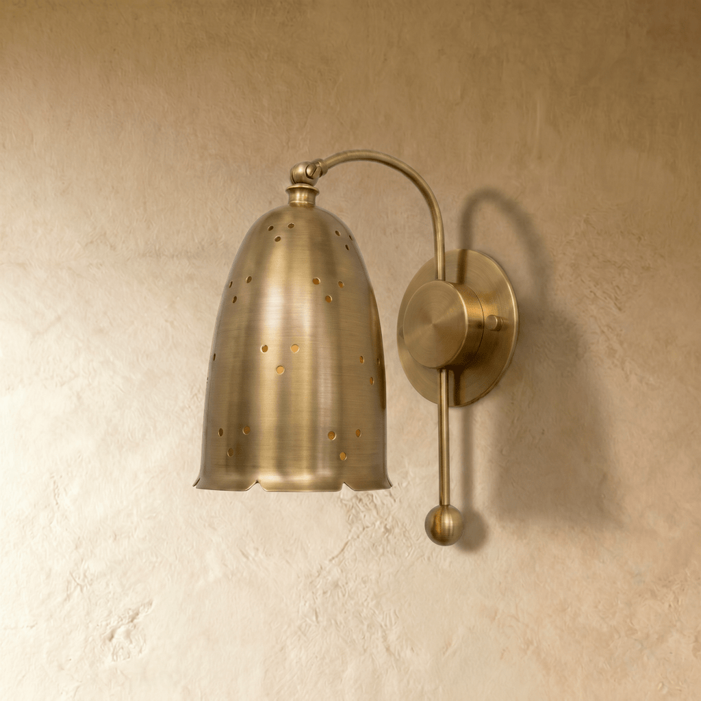 Clérachic wall lamp in brushed brass viewed close, star-like pinholes glowing through the bell shade.