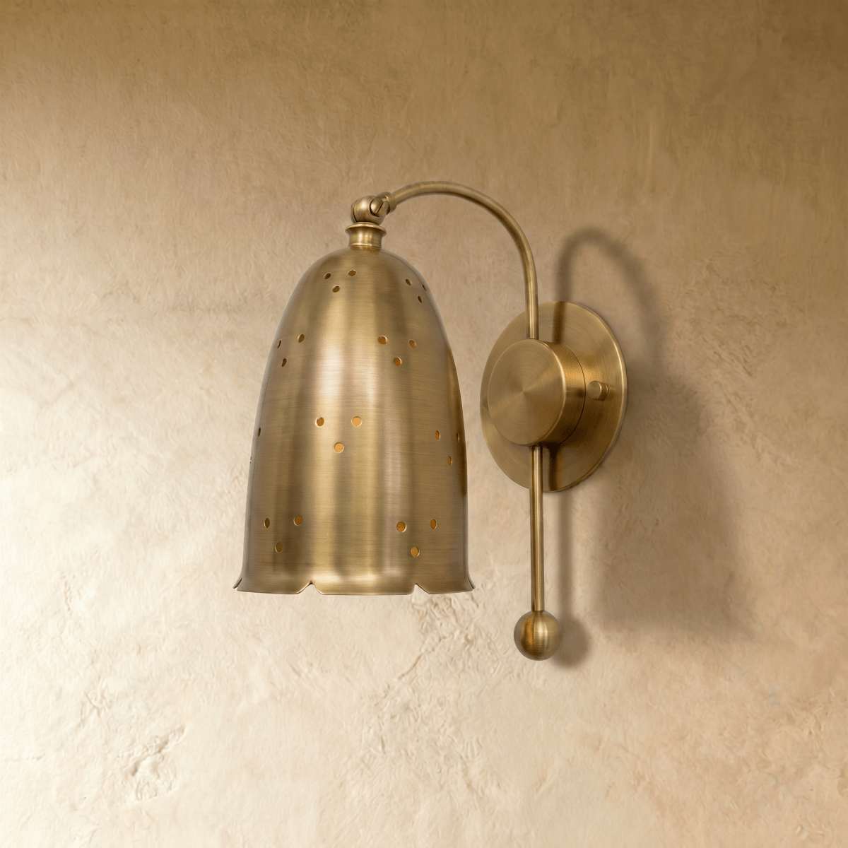 Clérachic wall lamp in brushed brass viewed close, star-like pinholes glowing through the bell shade.