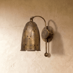 Clérachic wall lamp in vintage brass shown from another angle, pinholes glowing across the bell shade.
