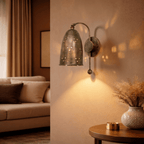 Clérachic wall lamp in vintage brass lighting a living room corner beside a sofa and dried-grass vase.