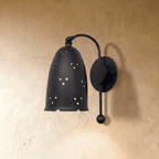 Clérachic wall lamp in matte black, a perforated bell shade glowing softly on a curved wall arm.