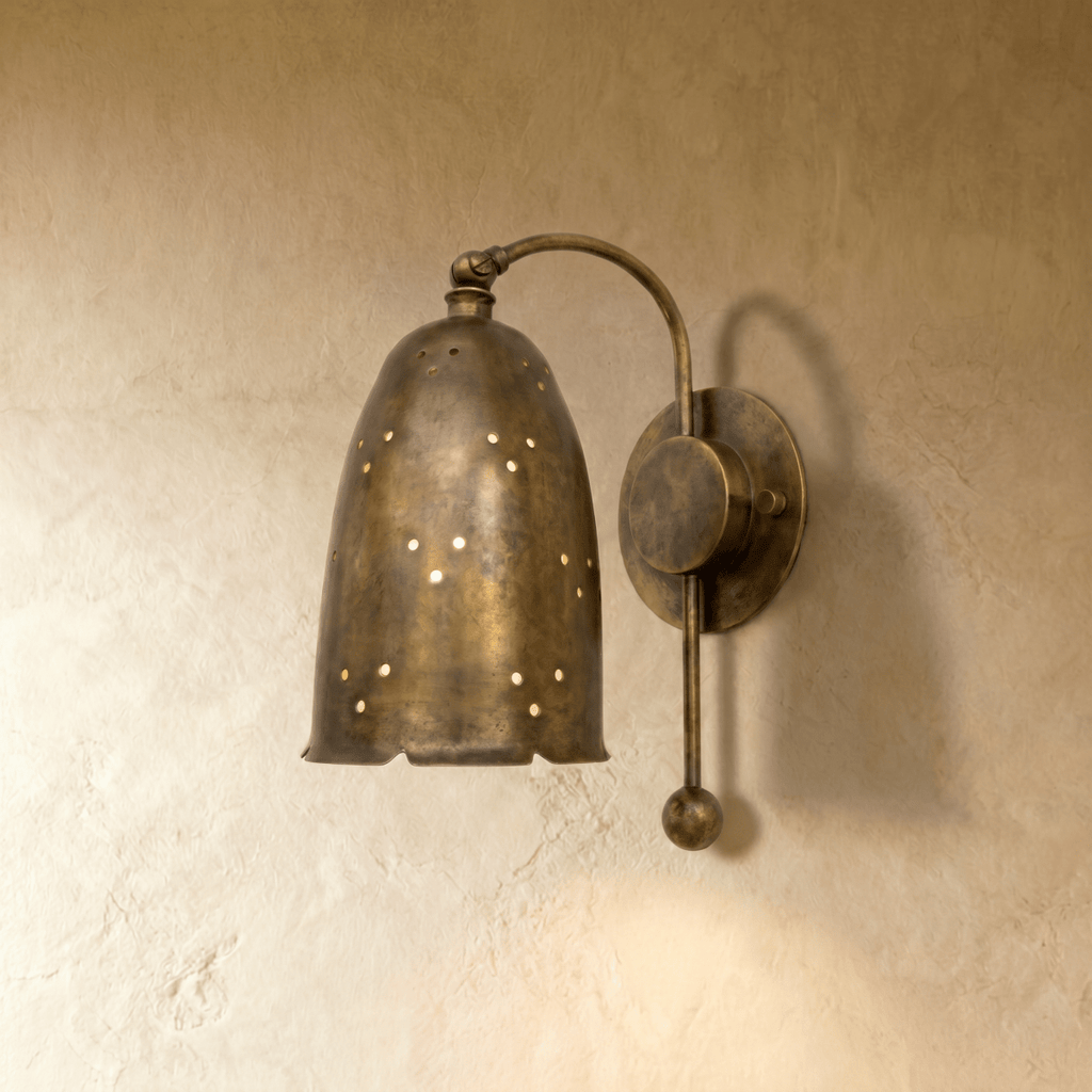 Clérachic wall lamp in vintage brass, a perforated bell shade on a curved arm against a plaster wall.