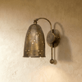 Clérachic wall lamp in vintage brass, a perforated bell shade on a curved arm against a plaster wall.
