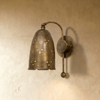 Clérachic wall lamp in vintage brass, a perforated bell shade on a curved arm against a plaster wall.