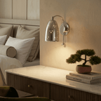 Clérachic wall lamp in chrome above a fluted dresser with a bonsai plant and stacked books.