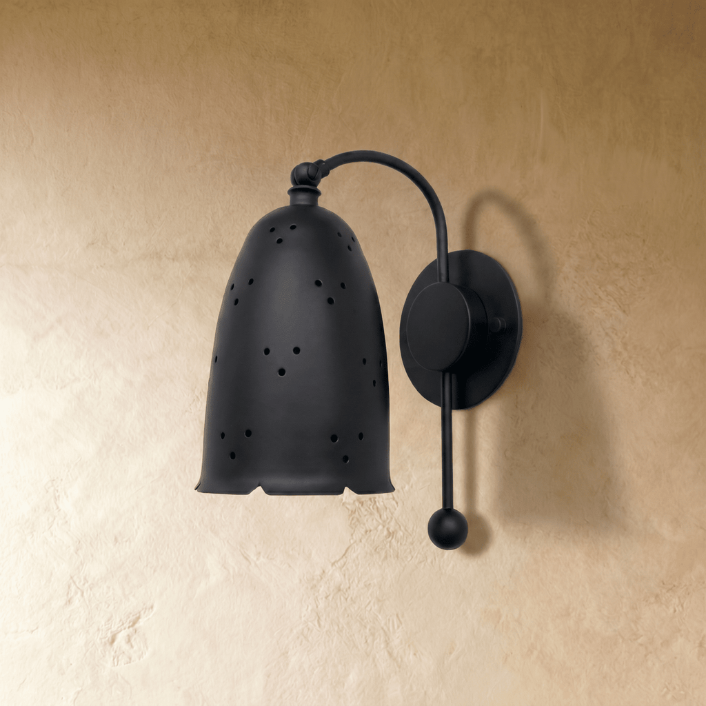 Clérachic wall lamp in matte black viewed close, star-like pinholes glowing through the bell shade.