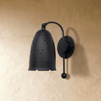 Clérachic wall lamp in matte black viewed close, star-like pinholes glowing through the bell shade.