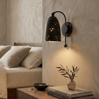 Clérachic wall lamp in matte black above a wooden nightstand with stacked design books and a vase.
