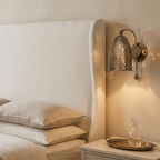 Clérachic wall lamp in vintage brass above a paneled headboard, beside a glass carafe on a tray.