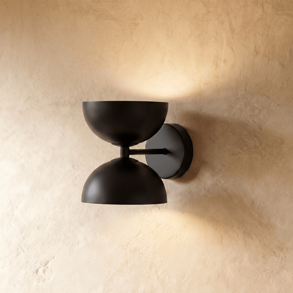 Clérachic double-dome wall sconce in matte black, mounted on a plaster wall and photographed straight-on in studio.
