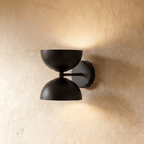 Clérachic double-dome wall sconce in matte black, mounted on a plaster wall and photographed straight-on in studio.