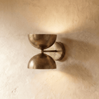 Clérachic double-dome wall sconce in vintage brass, mounted on a plaster wall and shown from a straight-on studio angle.