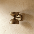 Clérachic double-dome wall sconce in vintage brass, photographed on a plain plaster wall from a slightly closer angle.