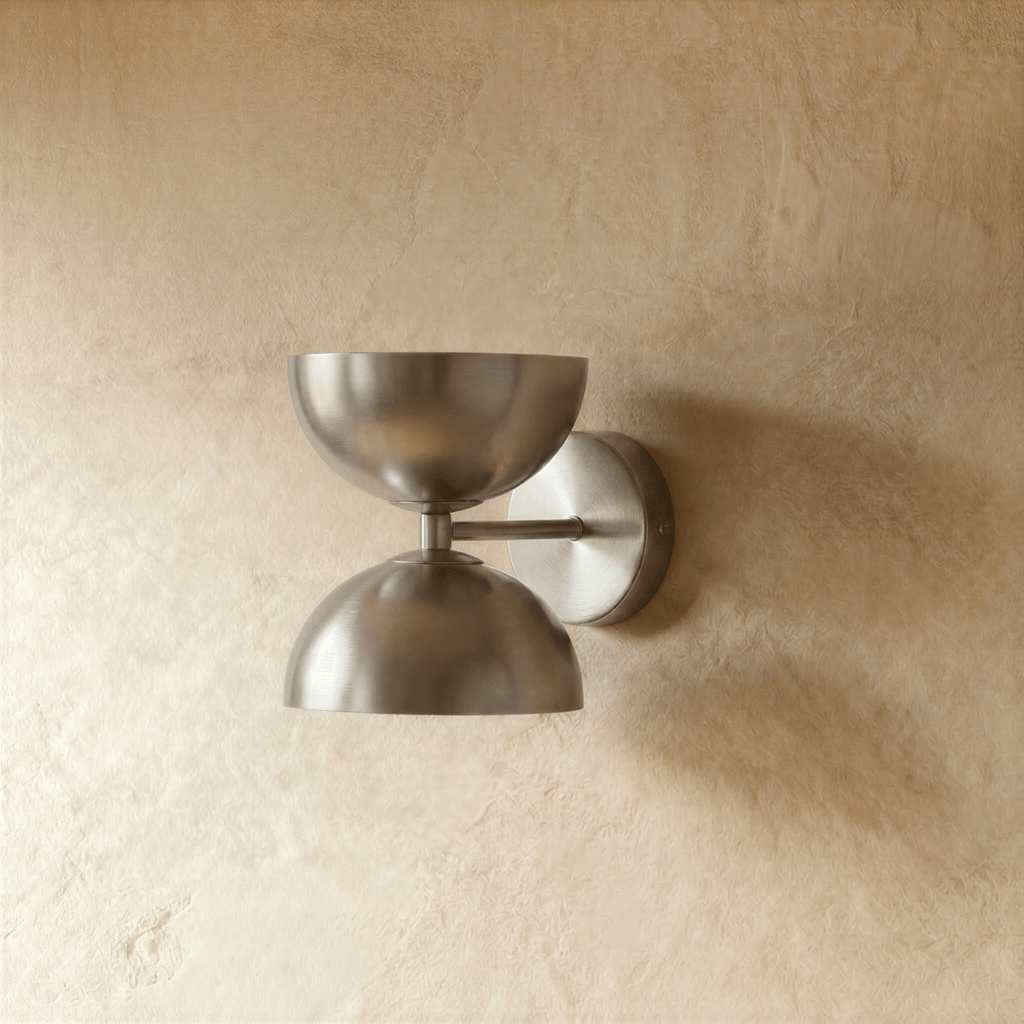 Clérachic double-dome wall sconce in brushed chrome, shown closer-cropped against a plain plaster studio wall.
