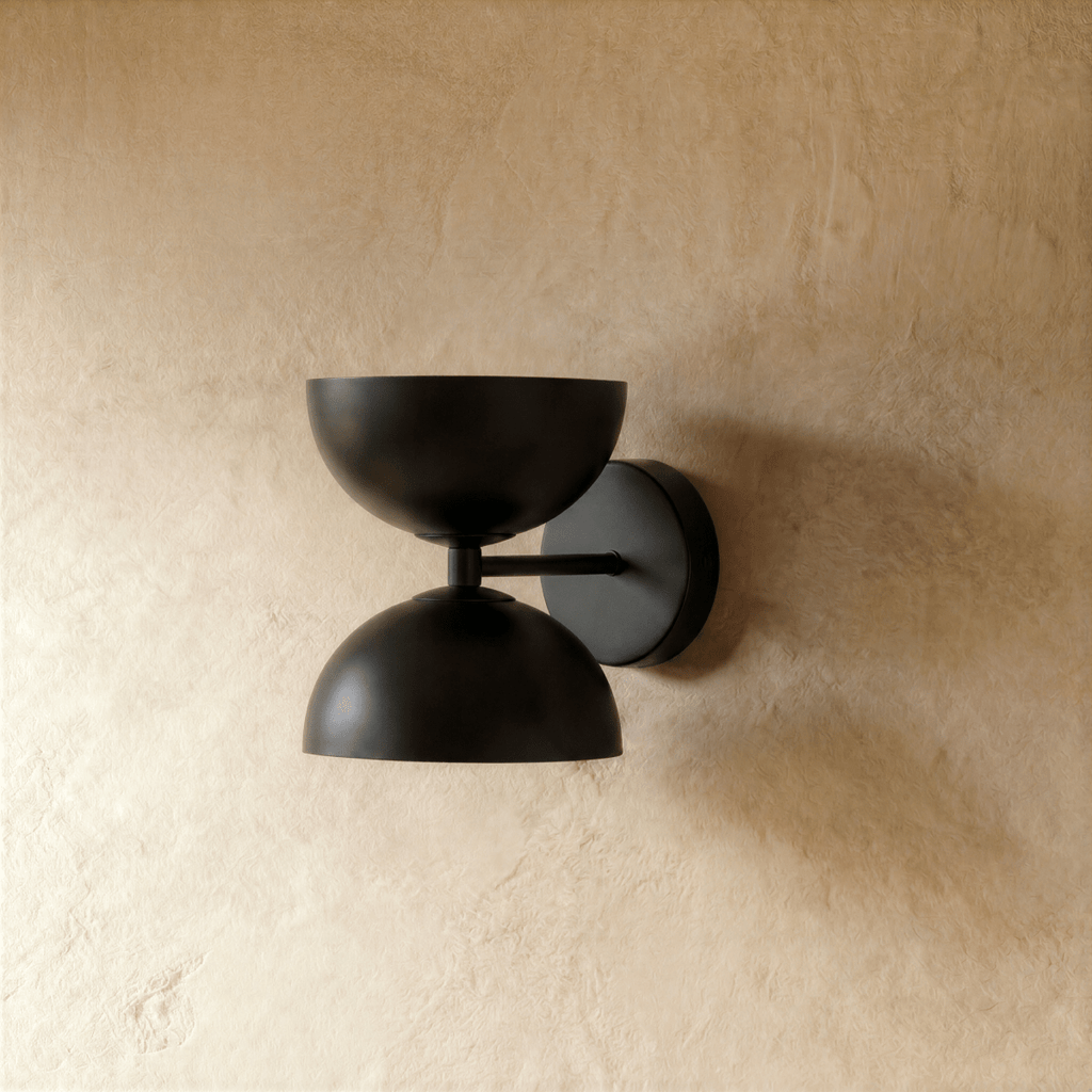 Clérachic double-dome wall sconce in matte black, shown closer-cropped against a plain plaster studio wall.