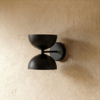 Clérachic double-dome wall sconce in matte black, shown closer-cropped against a plain plaster studio wall.
