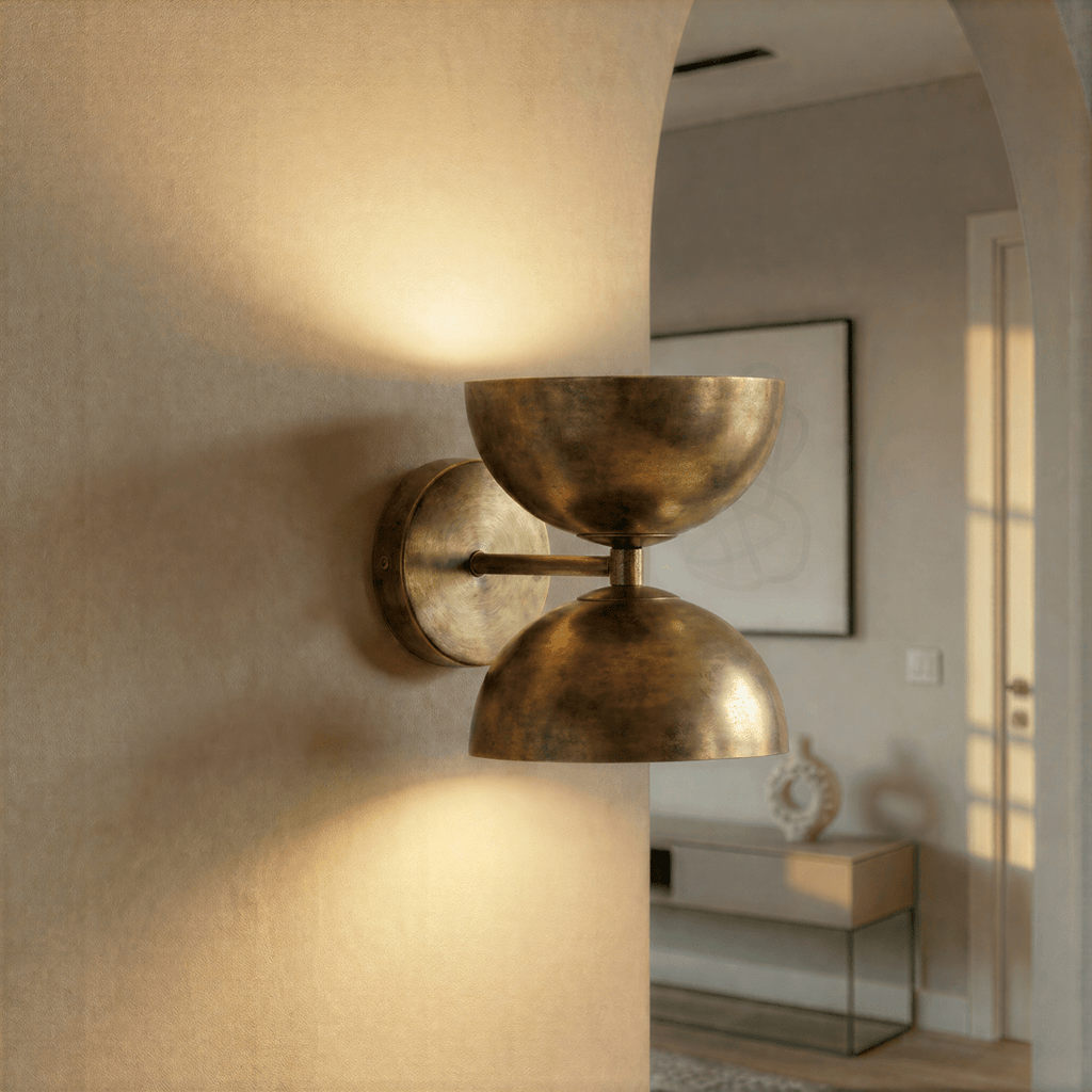 Clérachic vintage brass double-dome wall sconce lit on a hallway wall beside an archway into a living room.