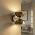Clérachic vintage brass double-dome wall sconce lit on a hallway wall beside an archway into a living room.
