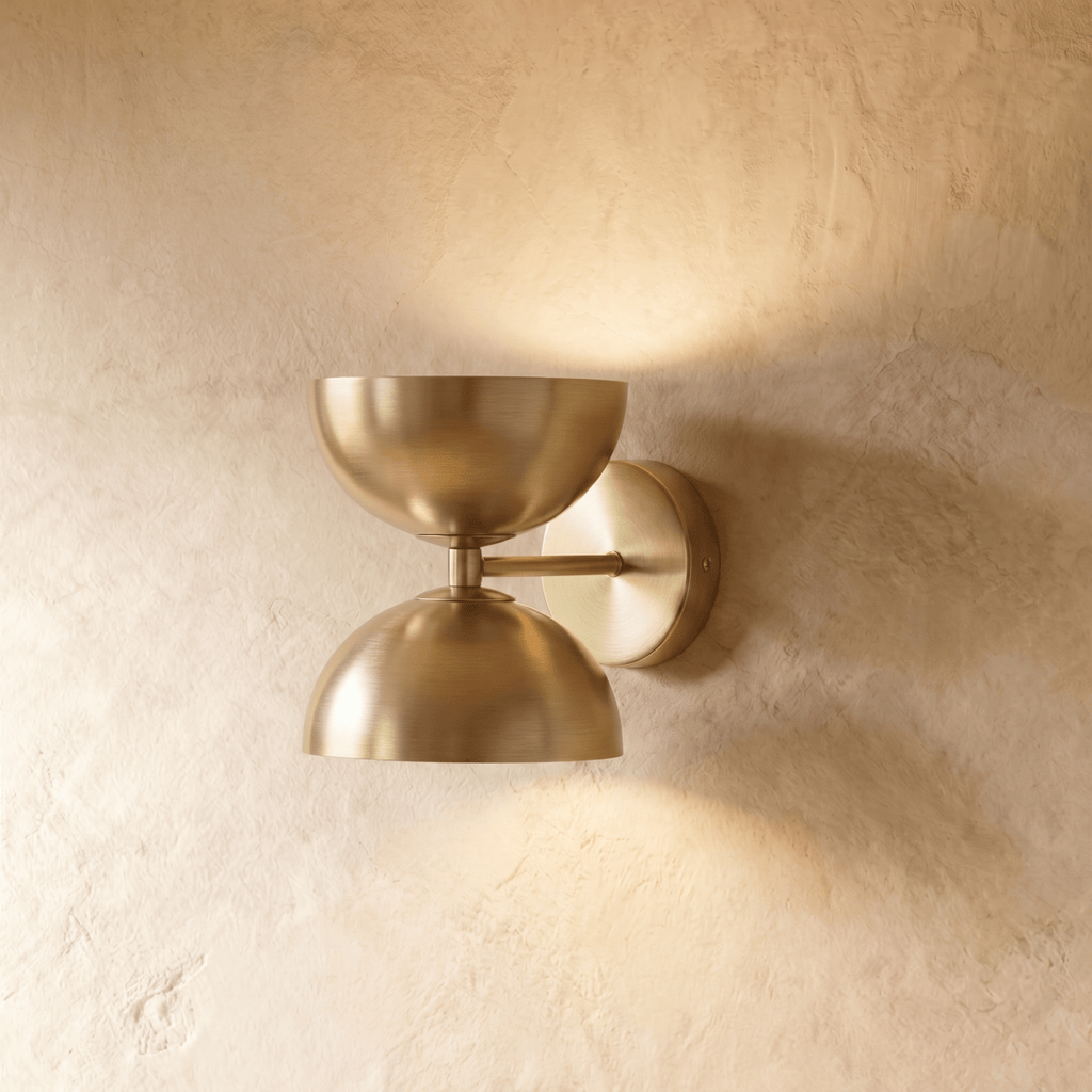 Clérachic double-dome wall sconce in polished brass, mounted on a plaster wall and photographed straight-on in studio.