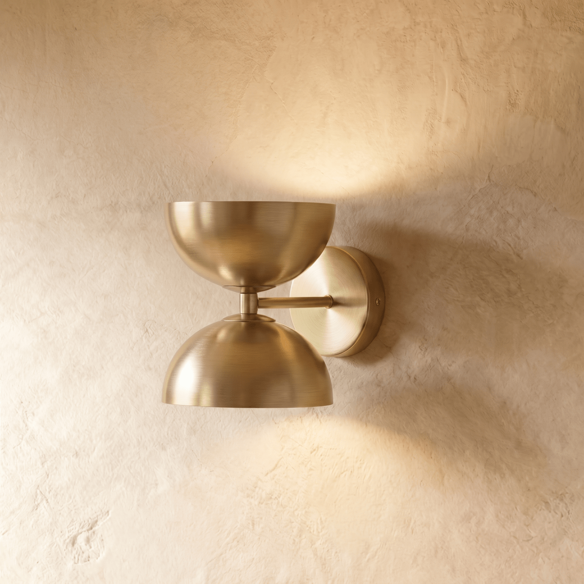 Clérachic double-dome wall sconce in polished brass, mounted on a plaster wall and photographed straight-on in studio.
