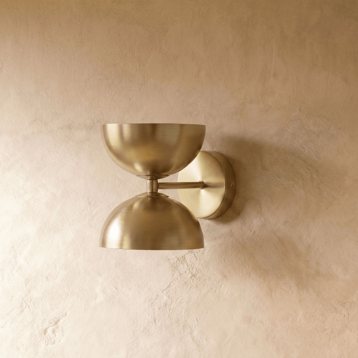 Clérachic double-dome wall sconce in polished brass, shown closer-cropped against a plain plaster studio wall.