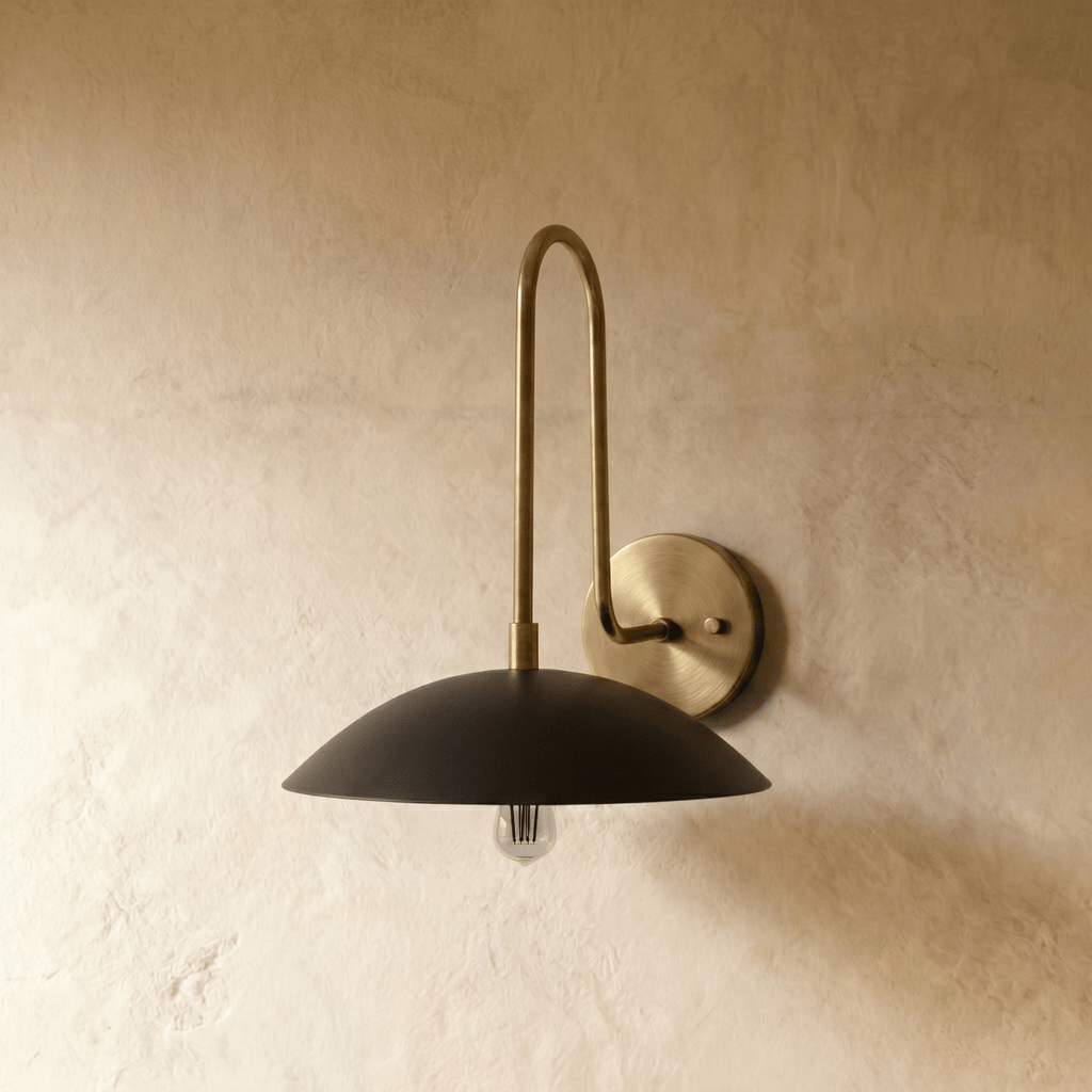 A chrome-finish Clérachic wall lamp with a black dome shade and warm exposed bulb, set against a plaster wall.