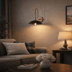 In a living room, this vintage brass Clérachic wall lamp lights a beige sofa corner with its black dome shade.
