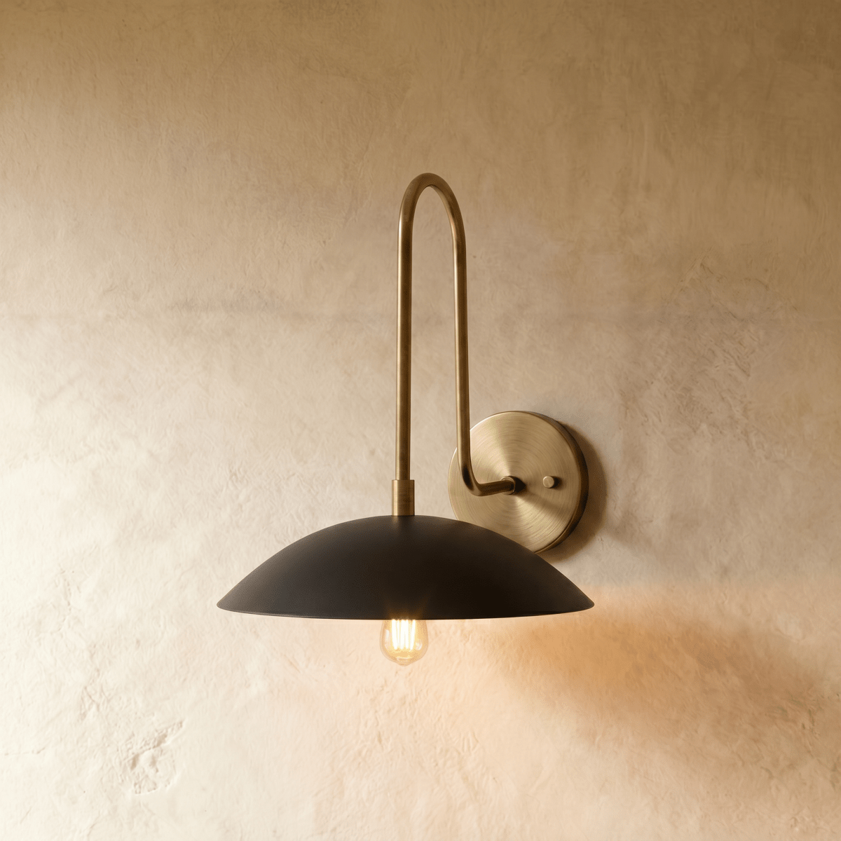 Clérachic wall lamp shown in polished brass, its gooseneck arm rising to a black dome shade over an exposed bulb.