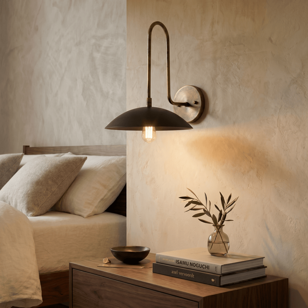 This vintage brass Clérachic wall lamp warms a bedroom nightstand stacked with books beside a small vase.