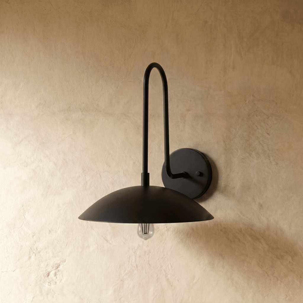 This all-black Clérachic wall lamp is shown straight on, its dome shade casting warm light from an exposed bulb.