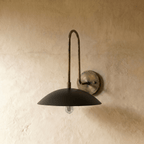 This vintage brass Clérachic wall lamp curves upward before ending in a wide black dome shade over a plaster wall.