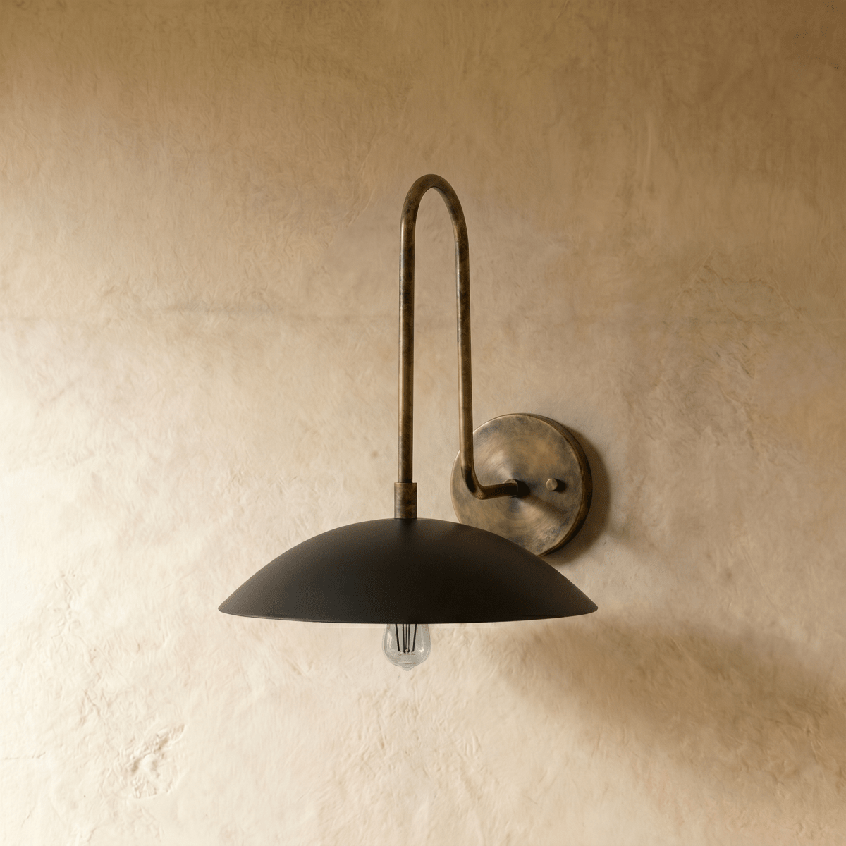 This vintage brass Clérachic wall lamp curves upward before ending in a wide black dome shade over a plaster wall.