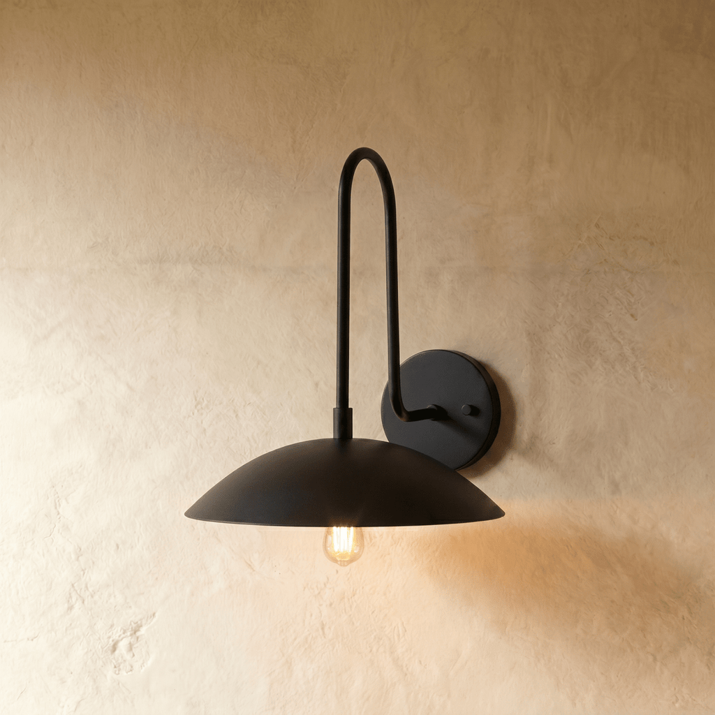 Clérachic wall lamp in matte black, arm and dome shade unified in one tone with a softly glowing bulb beneath.
