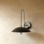 A closer view of the chrome Clérachic wall lamp, showing the join between its polished arm and black dome shade.