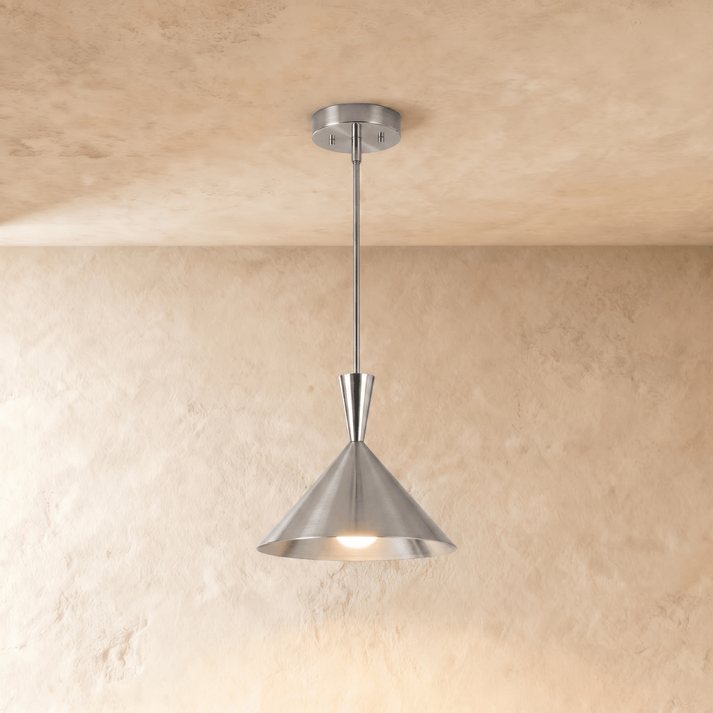 Clérachic cone-shade pendant light in a chrome finish, lit against a plaster wall, with the funnel neck between rod and cone clearly in view.