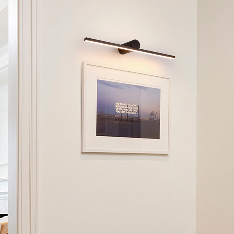 A lit Clérachic wall light glows above a white-framed photograph on a plain wall.