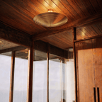 Clérachic ceiling light glowing in a sunlit wood-paneled hallway lined with glass and timber doors.