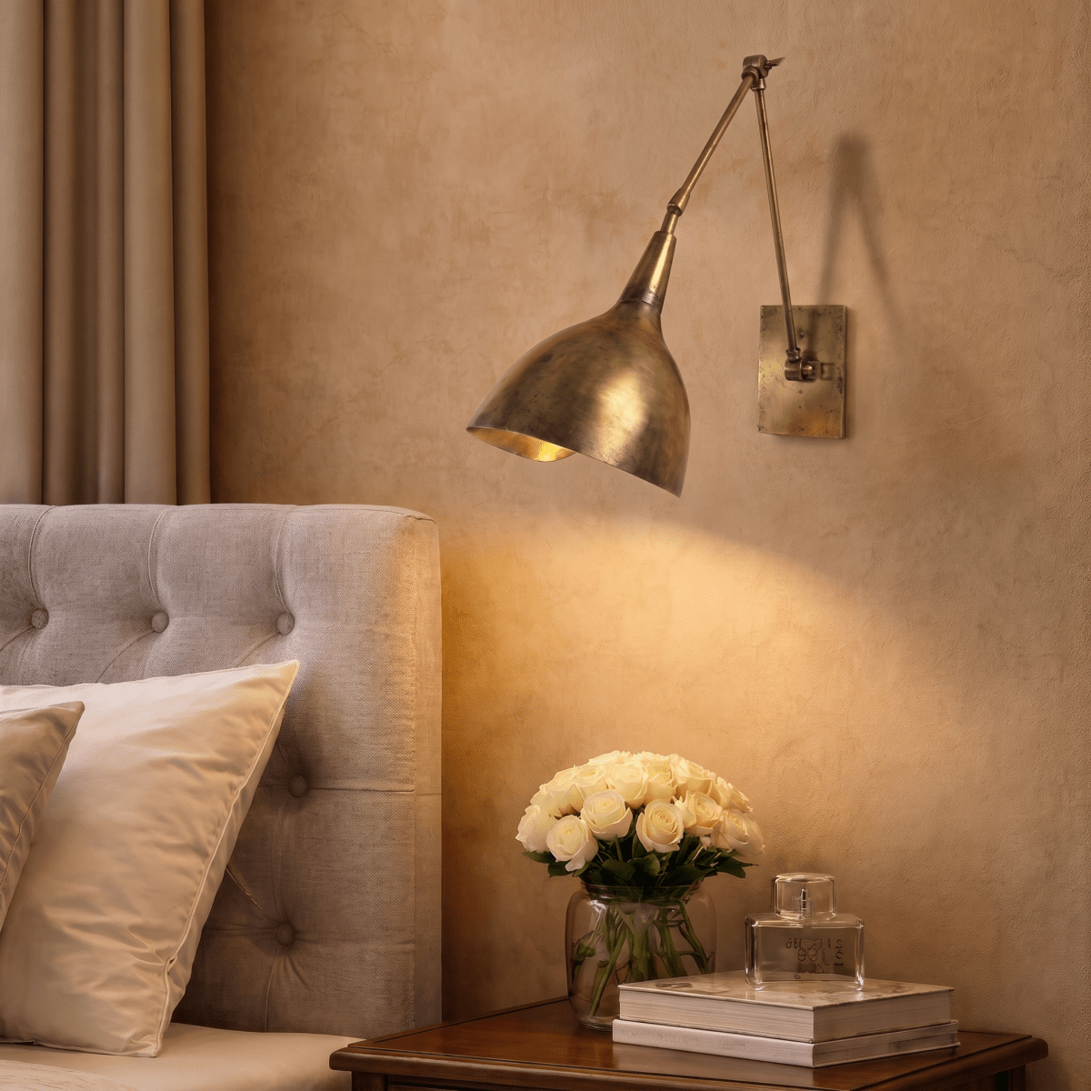 This vintage brass Clérachic wall lamp lights a bedroom nightstand holding white roses and a small bowl.