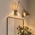 A vintage brass Clérachic wall lamp lights a round mirror and potted greenery near an entryway.
