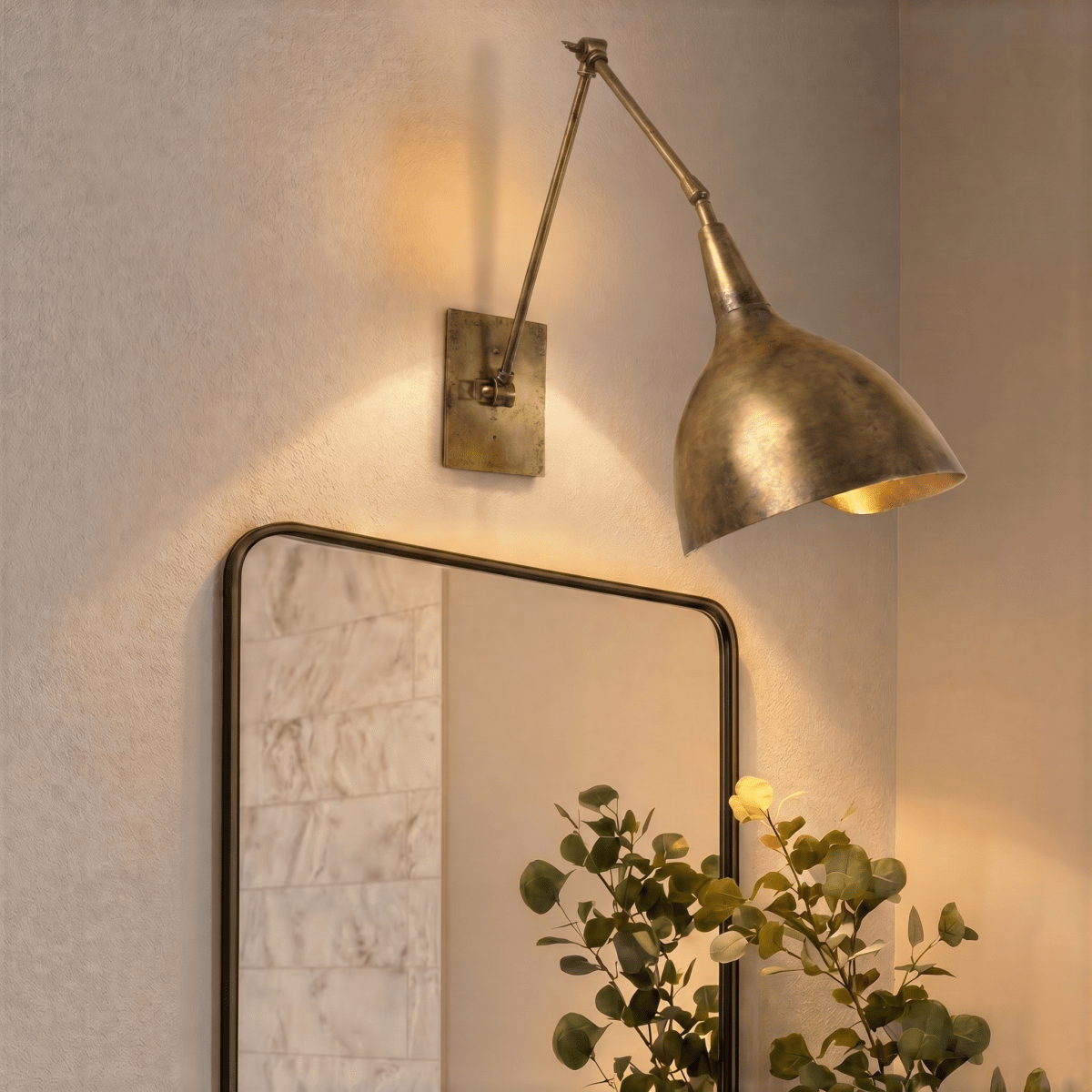 A vintage brass Clérachic wall lamp lights a round mirror and potted greenery near an entryway.