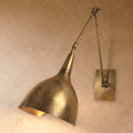 Clérachic wall lamp in vintage brass with a cone-shaped shade on an articulated swing arm against a plaster wall.