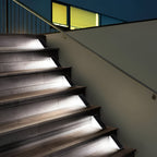The Clérachic step lights lit along dark timber stairs beside a glass balustrade.