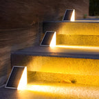 Three Clérachic step lights lit on sandstone steps beside a rendered wall.
