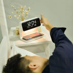 A hand reaching for the Clérachic bedside station's clock while a phone charges below.