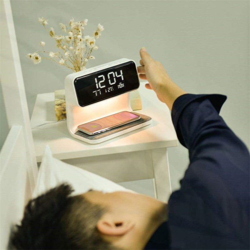 A hand reaching for the Clérachic bedside station's clock while a phone charges below.