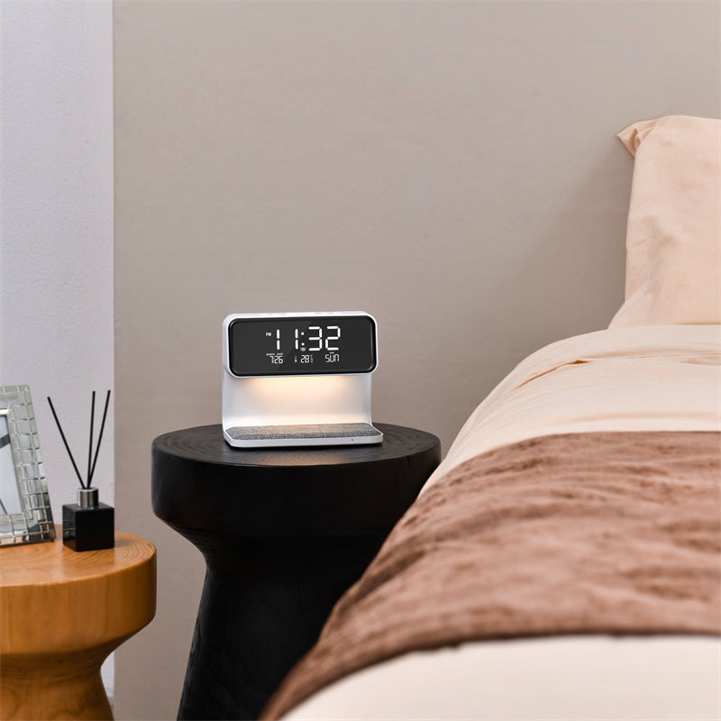 The Clérachic bedside station lit on a round black side table next to a made bed.